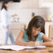 Young girl in kitchen doing homework with woman in background